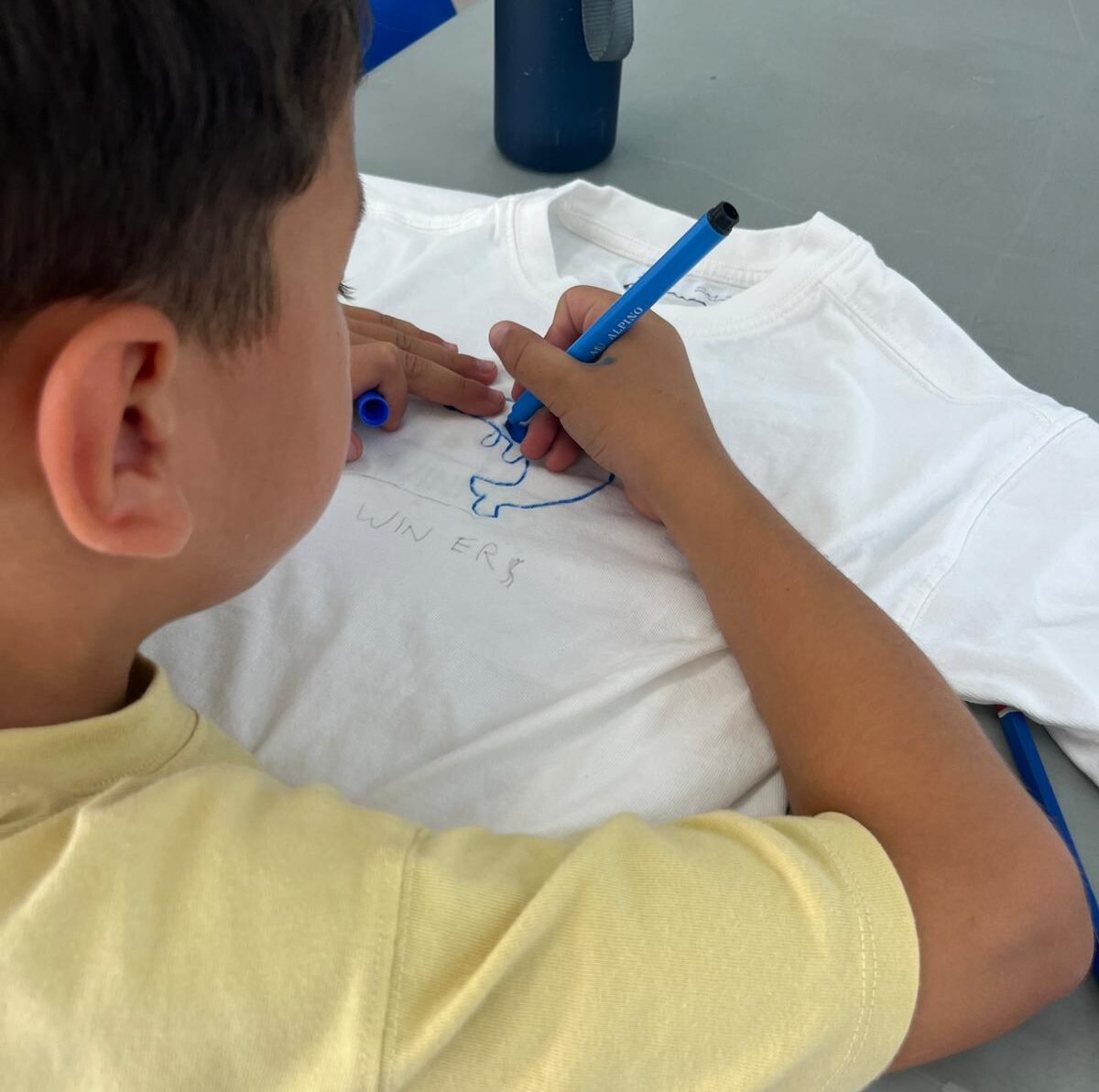 Niño pintando una camiseta durante un taller creativo de manualidades.
